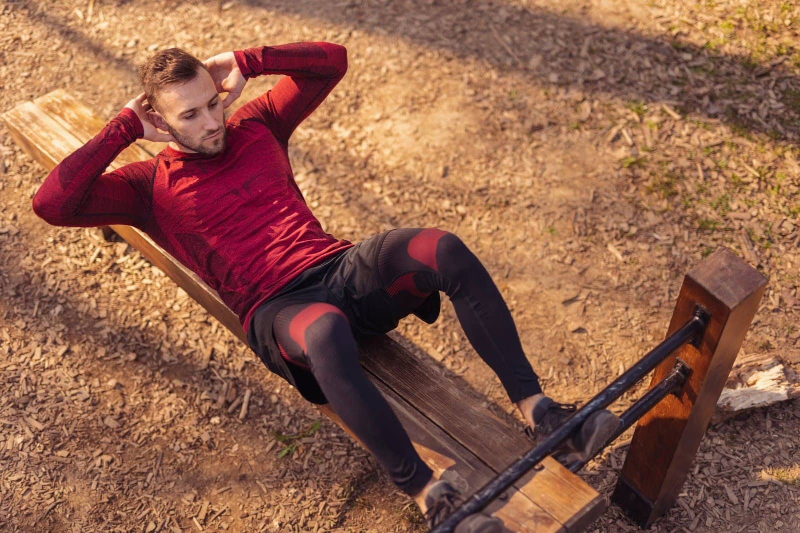 Man performing outdoor sit-ups on a wooden workout bench, focusing on core strength and fitness in natural surroundings.