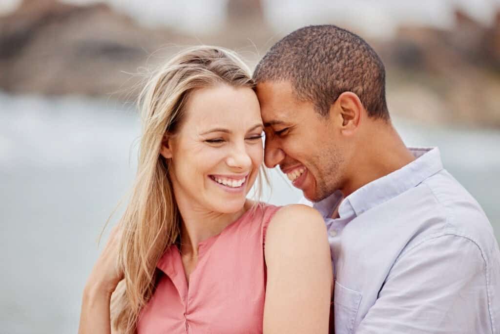 Happy couple embracing and smiling, sharing a tender moment outdoors by the beach.