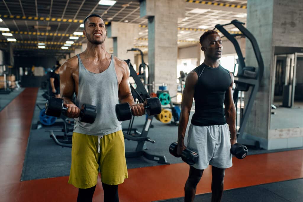 Testosterone and Aging: Unraveling the Role of Ashwagandha in Preserving Youthful Vitality || Two men lifting dumbbells in a gym, focusing on strength training and muscle building for physical fitness and endurance.