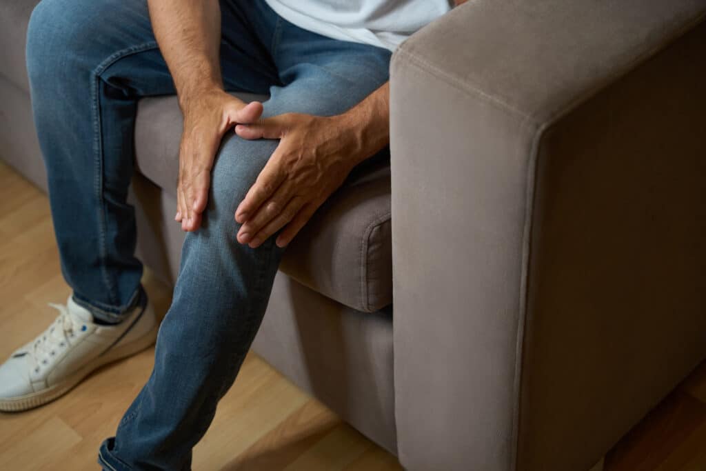 Man sitting on a couch with hands resting on his knee, highlighting knee pain or discomfort