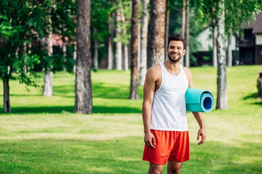 cheerful bearded man holding fitness mat in park. Is Tongkat Ali his secrete sauce?