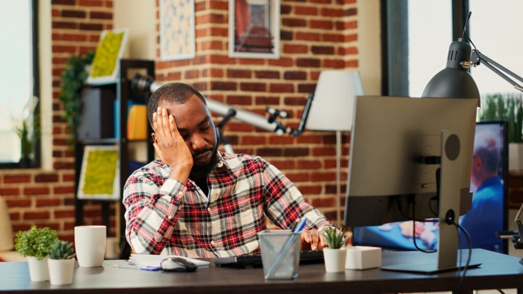 a man sitting at a desk with his head on his hand, tired and stressed. Is Ashwagandha his cure?