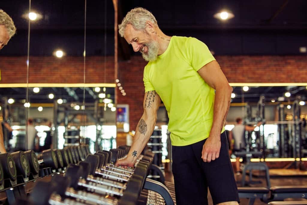 Older man at gym looking at the dumbells - could Maca root be his key to lifting that next heavy round?