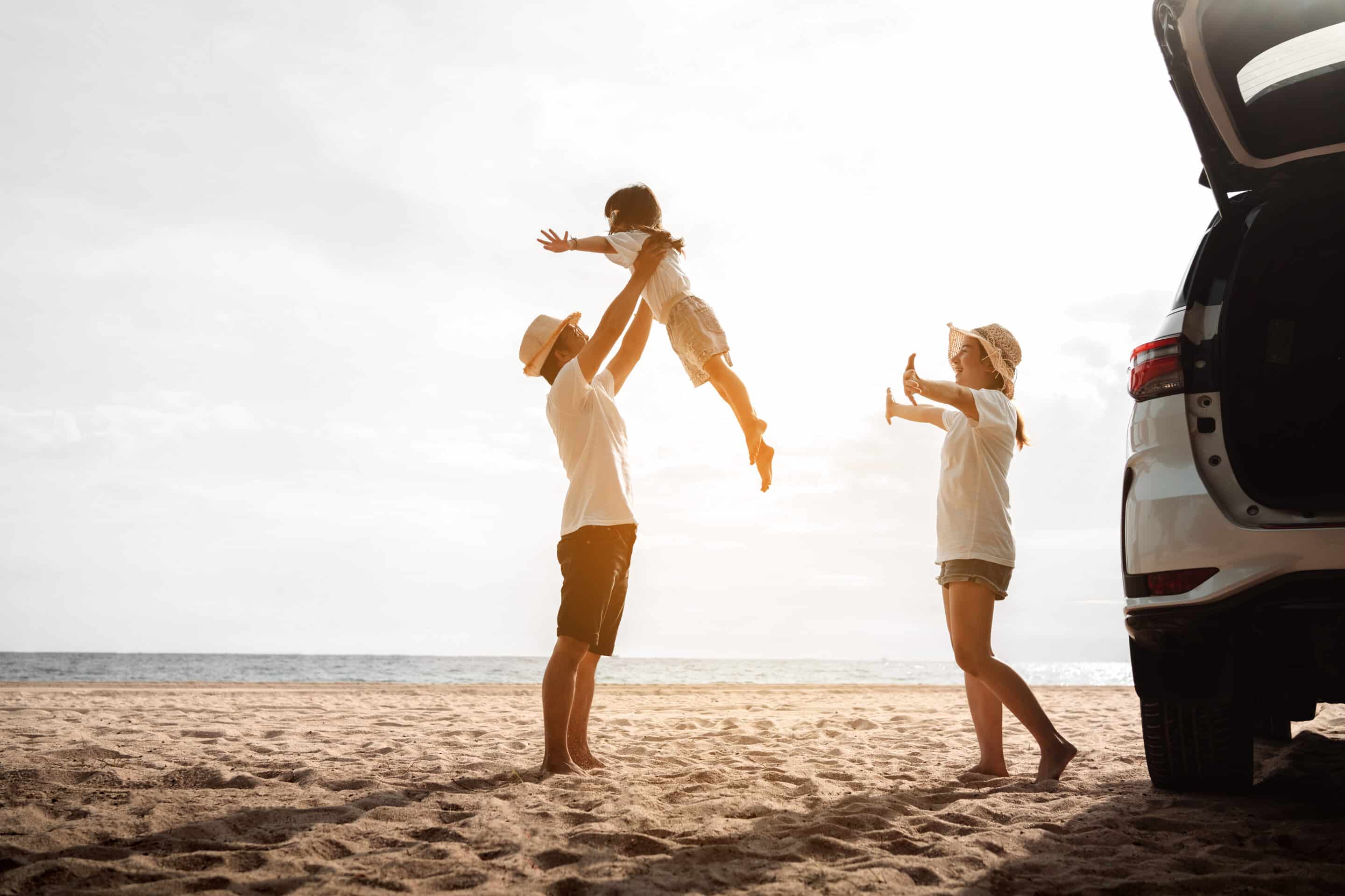 Dad lifting up daughter on beach with sunset and wife.  