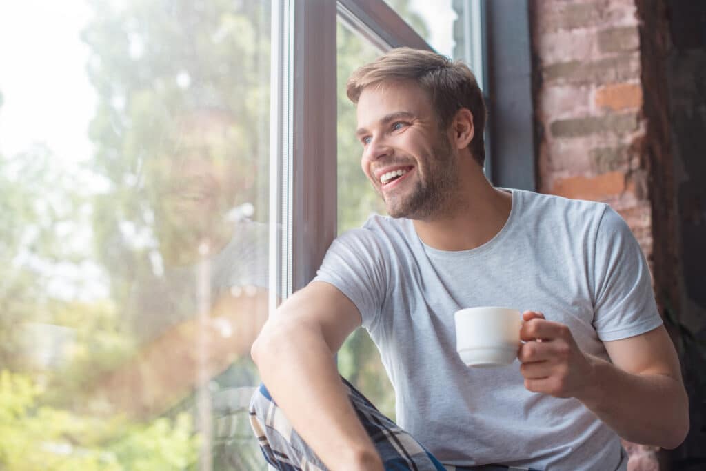 a man sitting by a window holding a cup of coffee after a great nights sleep using Valerian Root