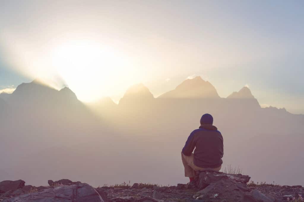 Man sitting calm watching the sun rise over the mountians: His serenity is from the Best Supplements to Reduce Stress