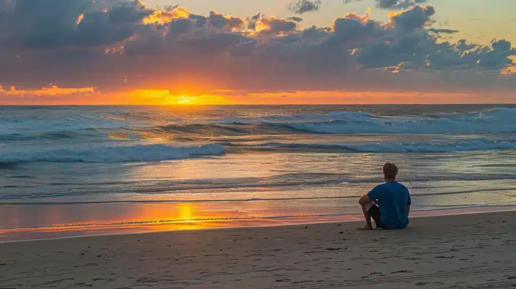 man sitting on beach calmly looking at sunrise due to taking natural anxiety and stress reliever