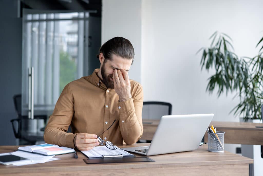 Businessman experiencing stress in workplace sitting at desk with laptop and papers. Thinking what could help him Ashwagandha vs L-Theanine.