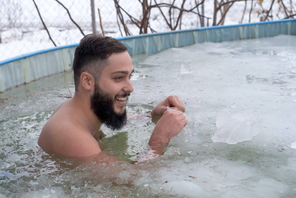 A young man smiling in a frozen family pool wondering which is better - a cold shower vs cold plunge