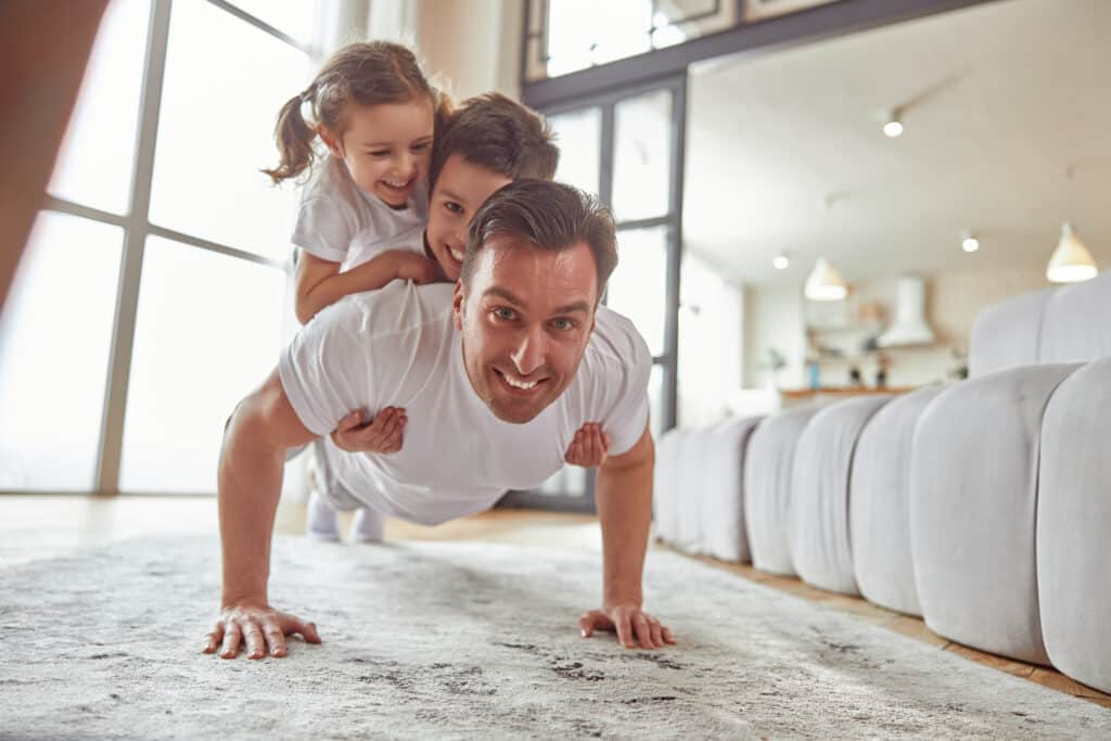 A father doing pushups with his two young kids laughing on his back showing strong bones from Vitamin D3 and K2 Benefits