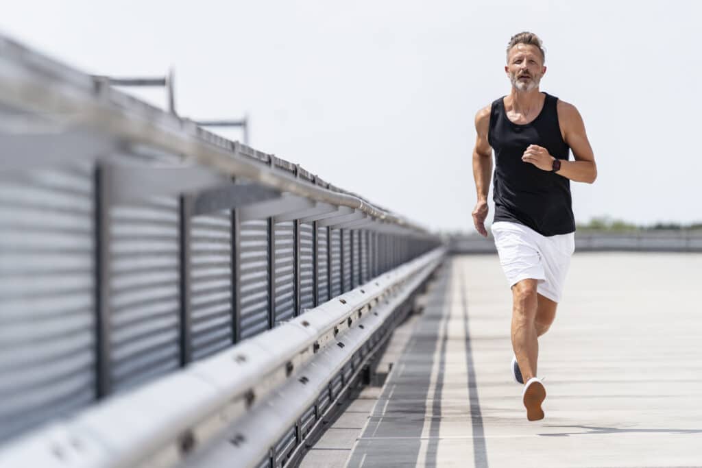 A man actively running down the street in gym shorts and tank top, along a bridge overlooking water. He gets his extra energy from supplements for better sleep, including Ashwagandha.