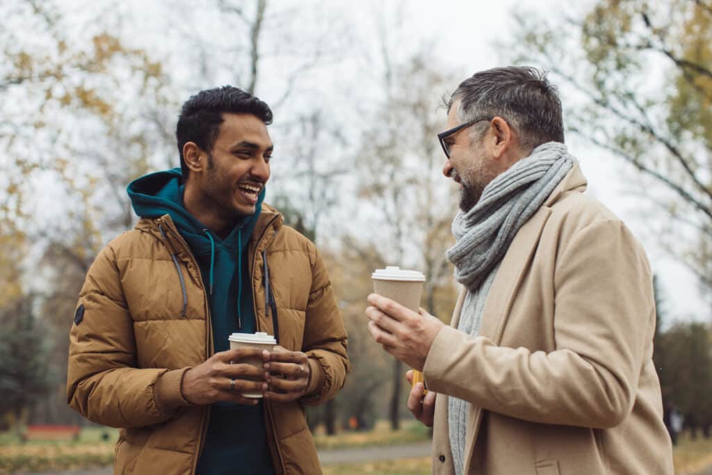 Two men in winter clothes in a park drinking coffee discussing mental quotes for men