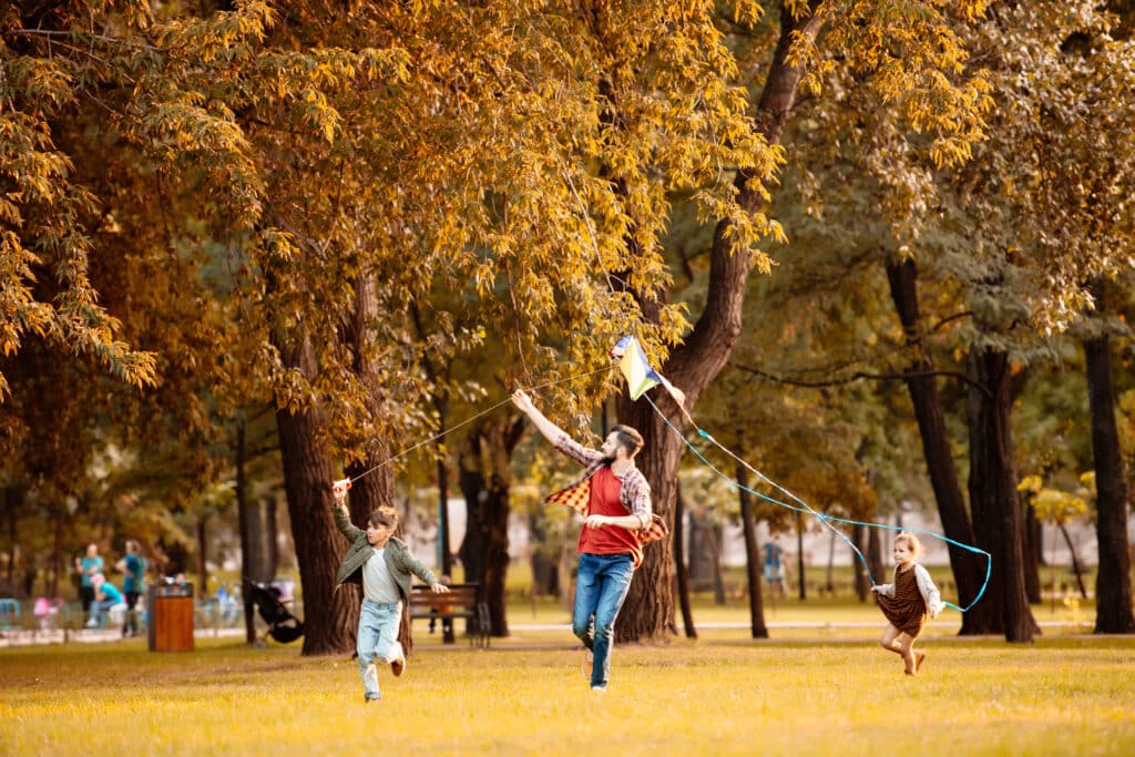 Father and two children running across the autumn park and flying a kite. is this exercise or a workout?