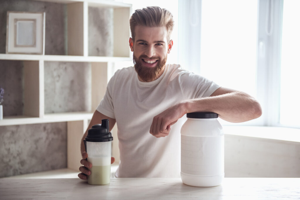 A young white man at kitchen counter and just mixed a protein shake with creatine benefits. Room is bright and sunny.