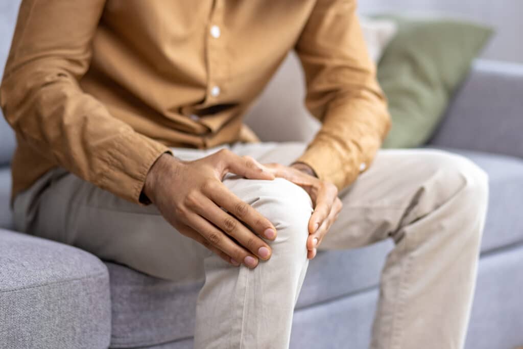 A man sitting on a couching rubbing his knee due to aching joint pain. Could supplementing with Boron improve this aching joint pain?