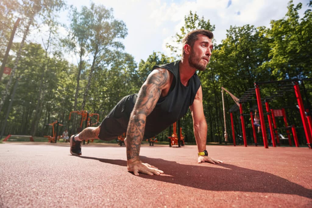 Supporting adaptogens for athletes, male athlete doing pushups in an outdoor park training area.