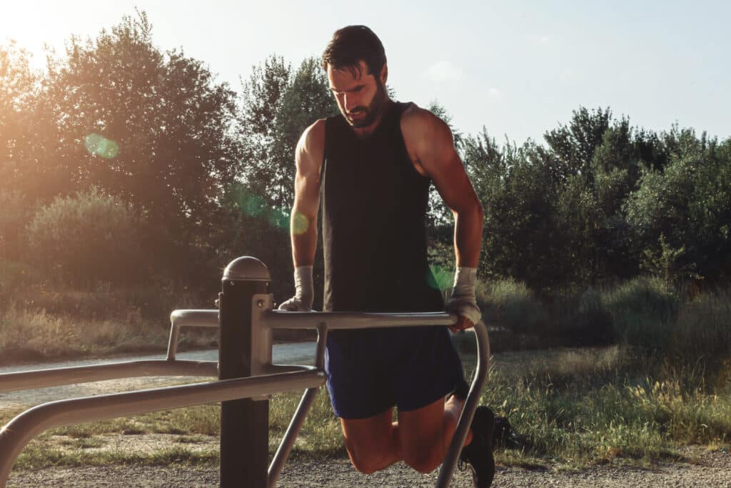 Fit white man in tanktop completing dips on outdoor gym in park on a sunny day. Maximizing Ashwagandha Muscle Building with fitness with age